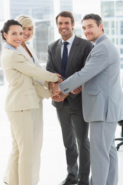 Portrait of business team joining hands together in a bright office